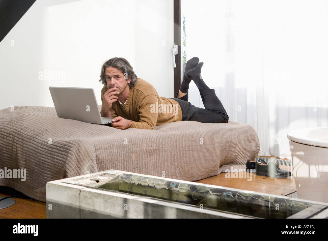 Un uomo disteso su un letto e utilizzando un computer portatile Foto Stock