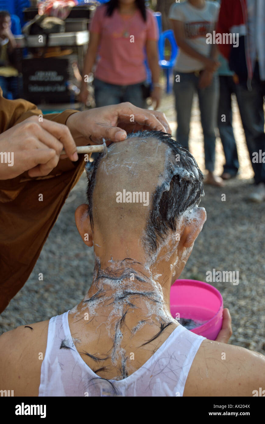 Thai monaco buddista utilizza un rasoio per rasatura della testa di un giovane uomo tailandese, parte dell'ordinazione di un monaco novizio Foto Stock
