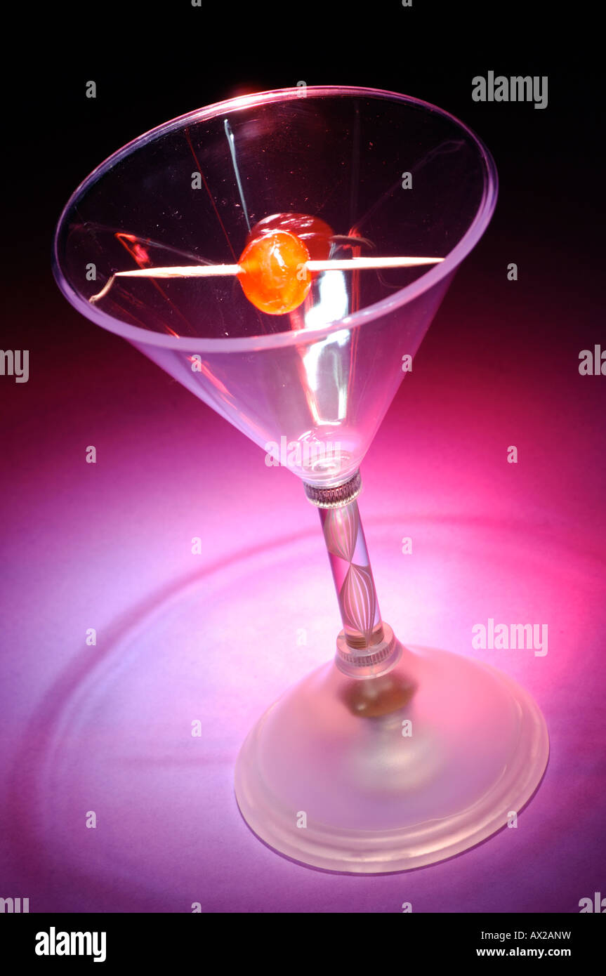 Un bicchiere da cocktail con un bastone e ciliegia glace angolata in un modo unusuak e in un viola malva lo sbiadimento del colore a nero Foto Stock