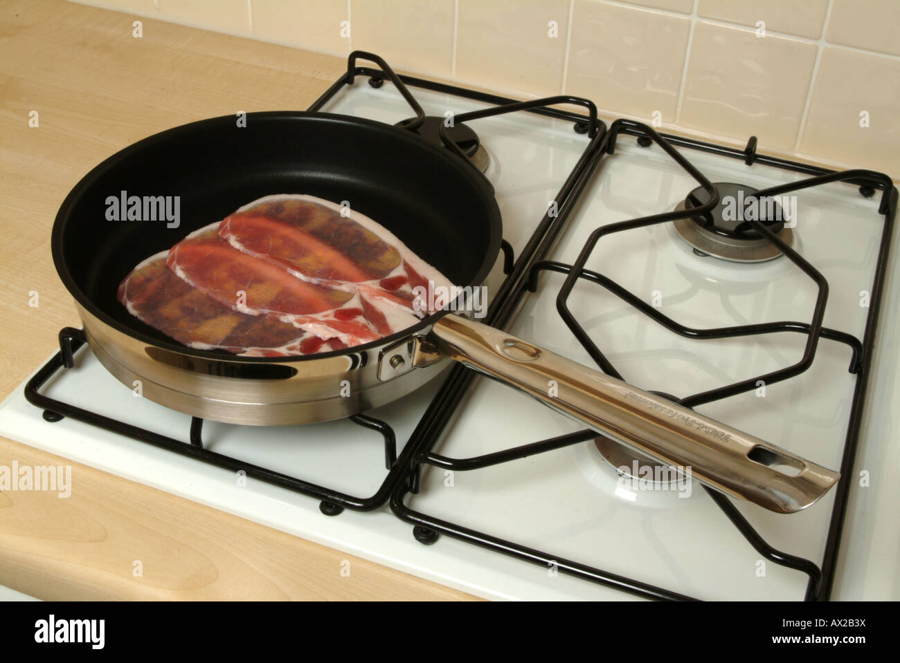 Il bacon in una padella con il manico di metallo su un piano cottura a gas.il manico di metallo è un buon conduttore di calore Foto Stock