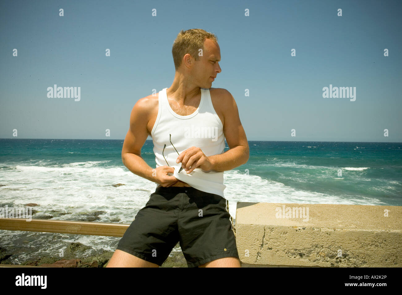 Uomo che pulisce i suoi occhiali da sole sul mare Foto Stock