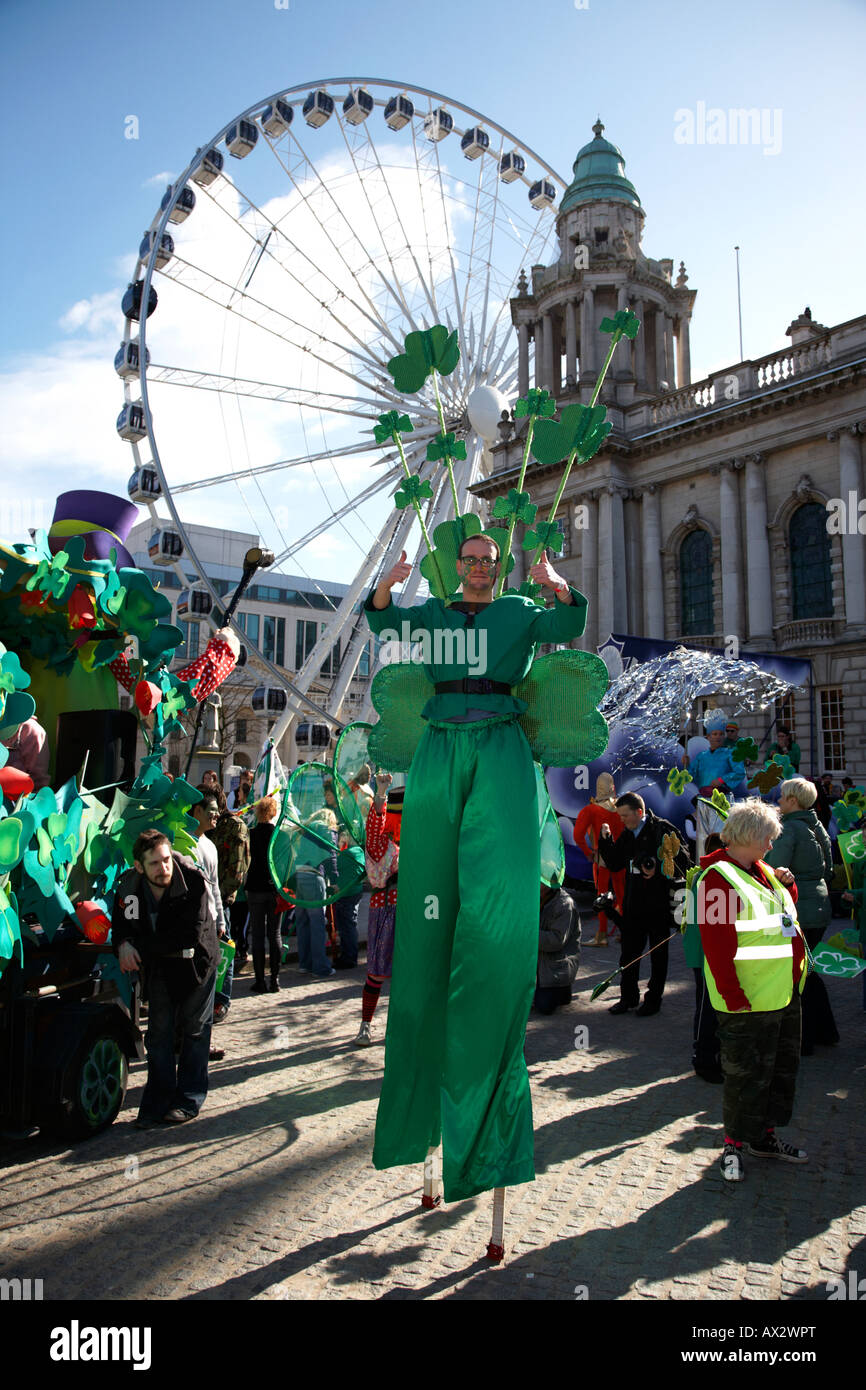 Stiltwalker vestito di verde che indossa trifogli a Belfast City Hall e la grande ruota prima della sfilata di carnevale e il giorno di San Patrizio Foto Stock