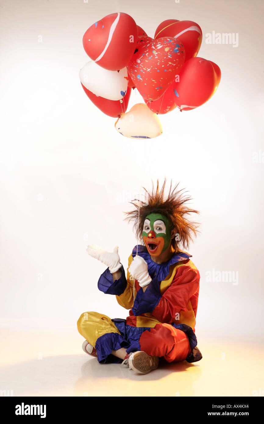 Ritratto di un joker seduto sul pavimento e palloncini di contenimento Foto Stock