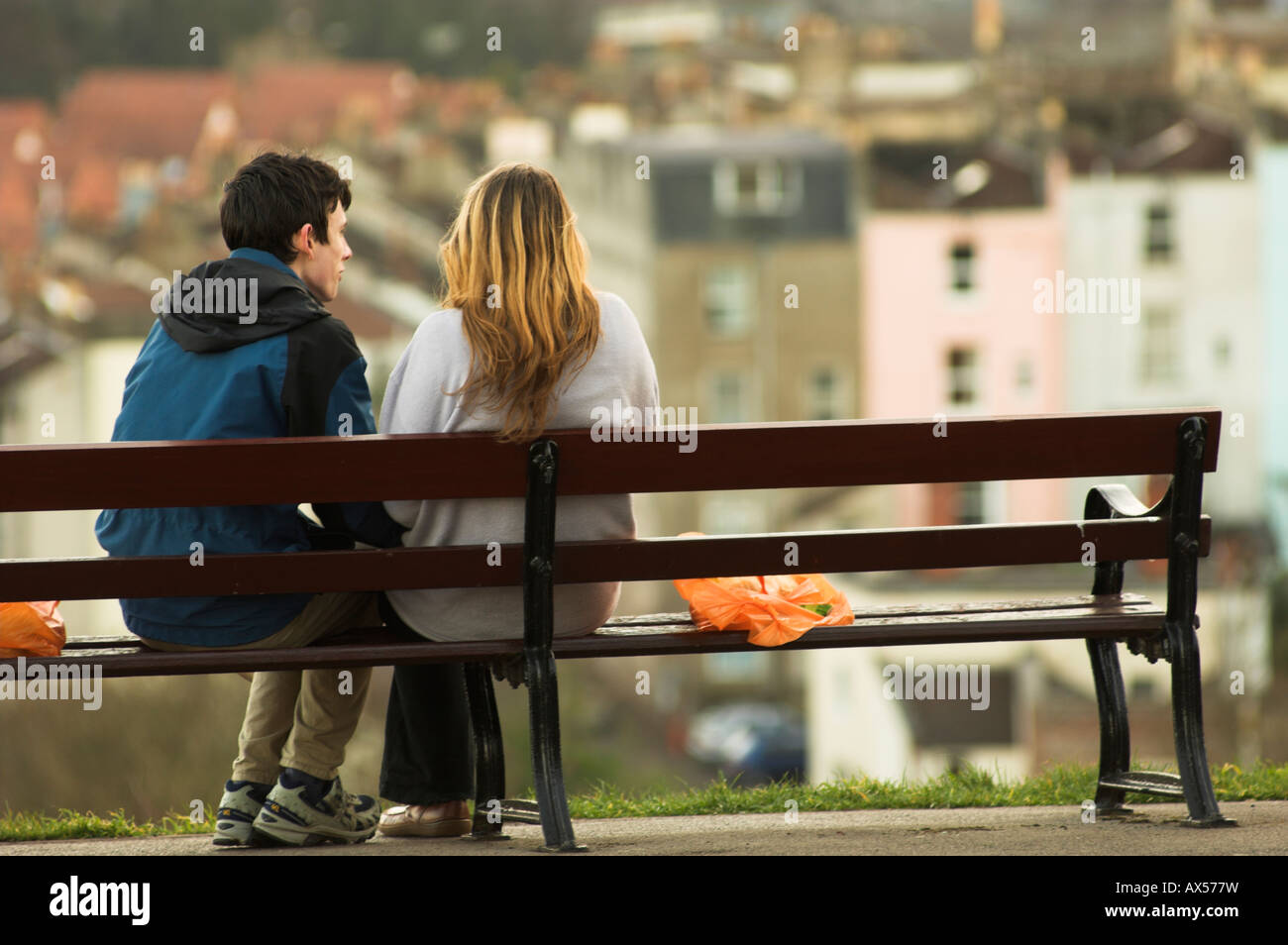 Coppia seduta in legno su una panchina nel parco in inverno sullo sfondo di case sfocato nella distanza Foto Stock