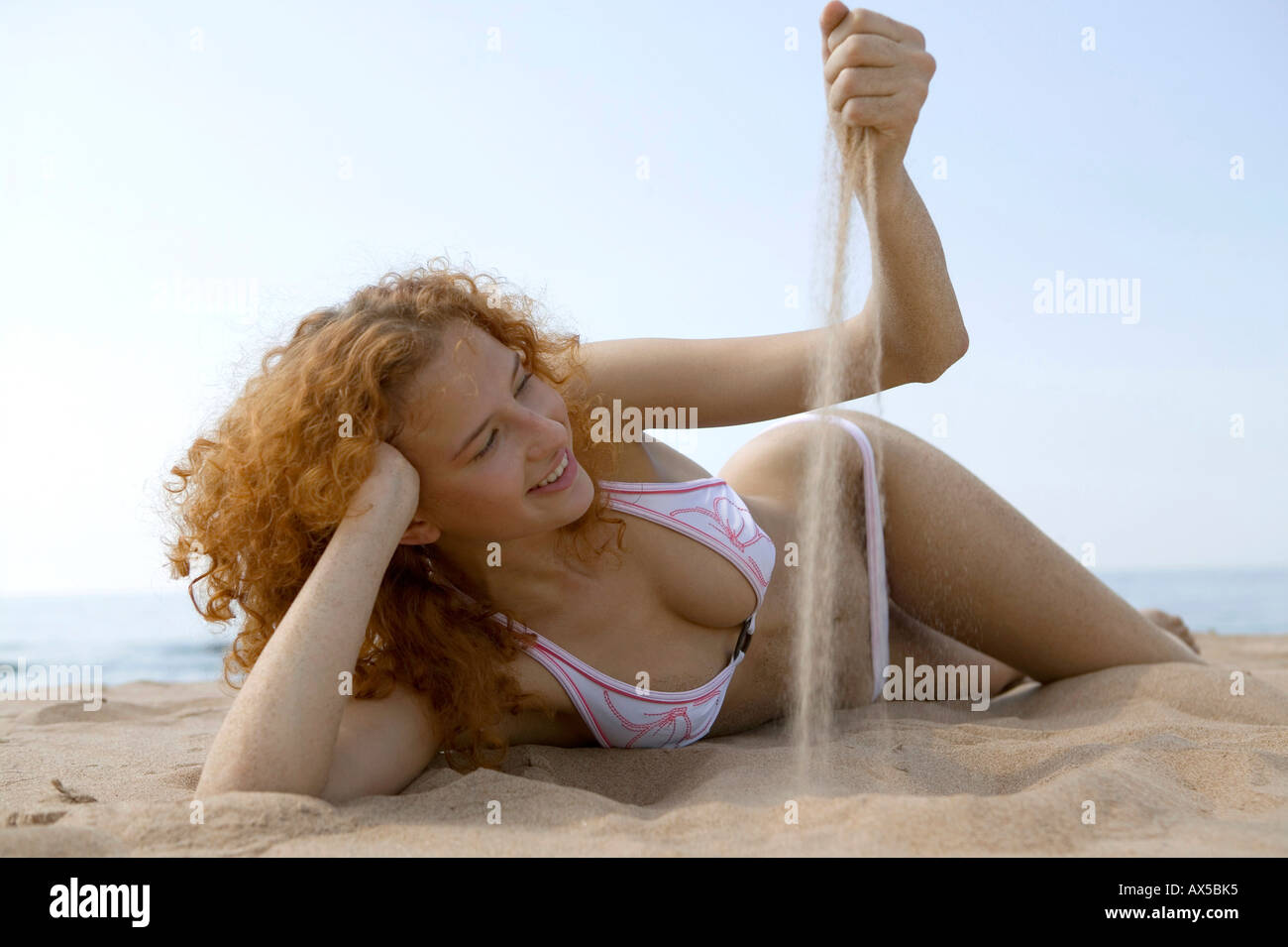 Giovane donna sdraiata sulla spiaggia, giocando con sabbia Foto Stock
