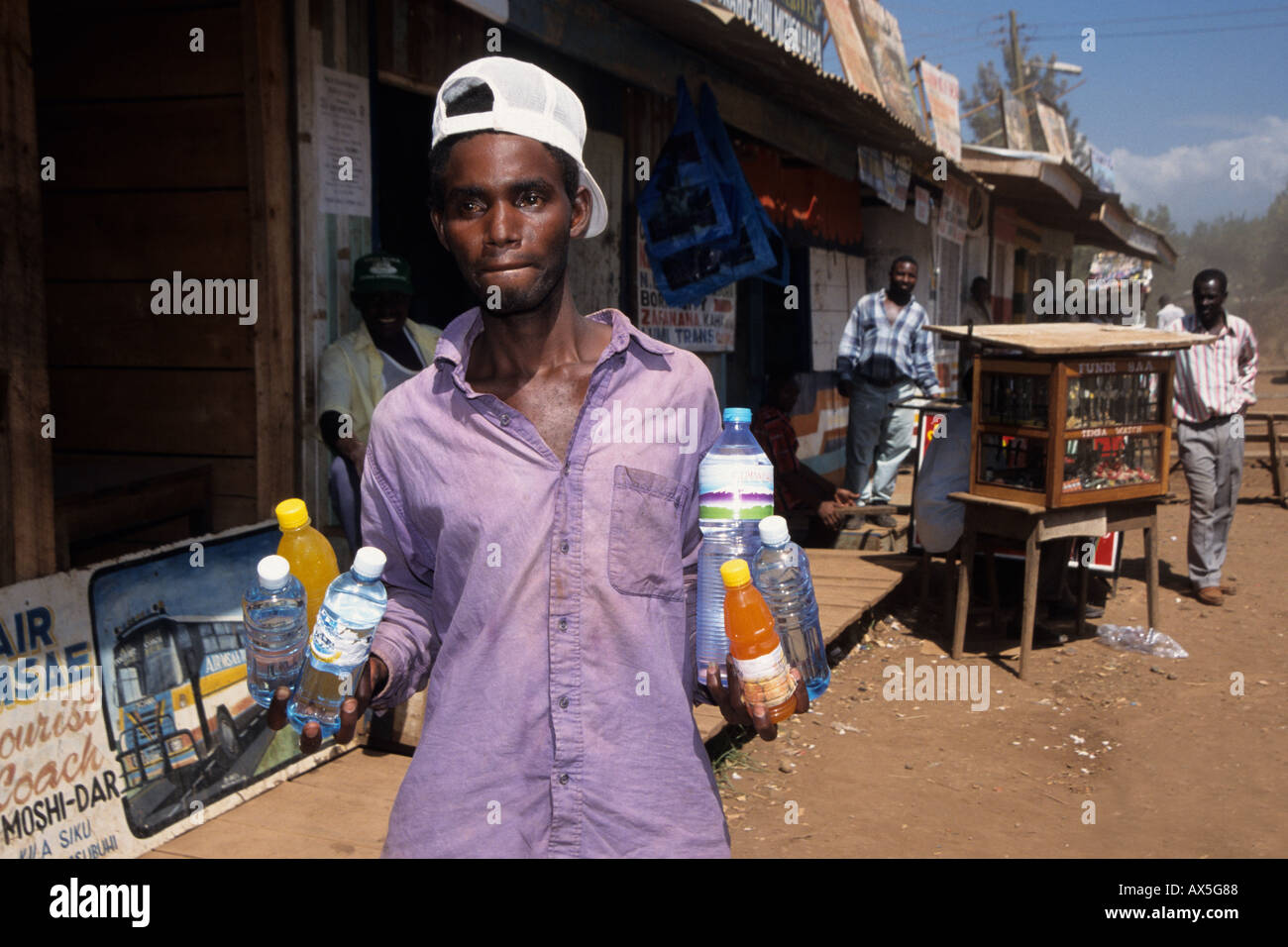 Giovane uomo che lavora come venditori ambulanti vendono bibite rinfrescanti presso una stazione degli autobus, Moshi, Tanzania Foto Stock