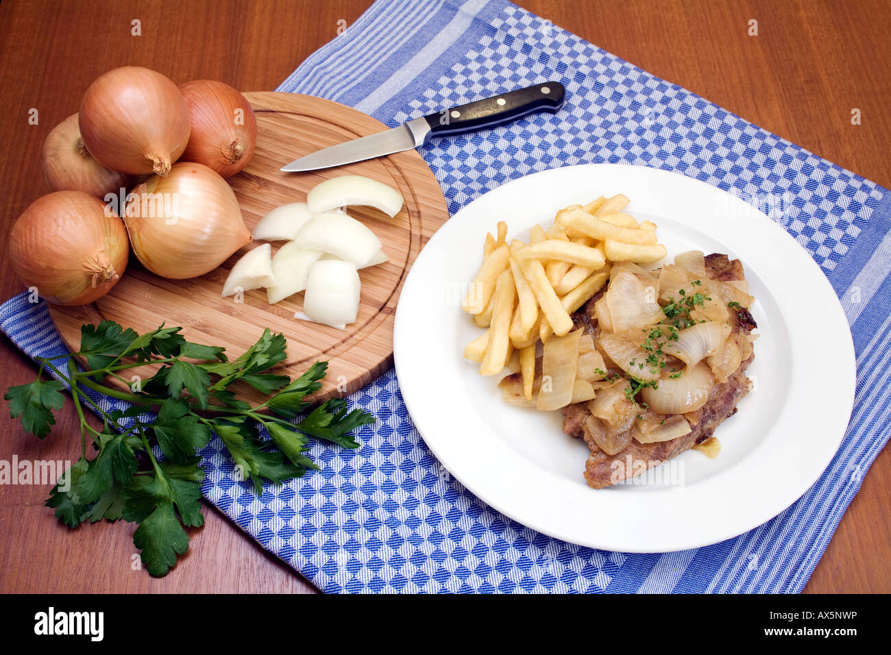 Bistecca di carne di maiale con cipolle arrosto e patatine fritte, intero e le cipolle tagliate a fette con un coltello su un tagliere Foto Stock