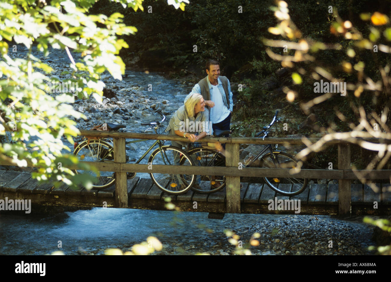 Giovane con le biciclette, in piedi sul ponte di legno, sorridente Foto Stock