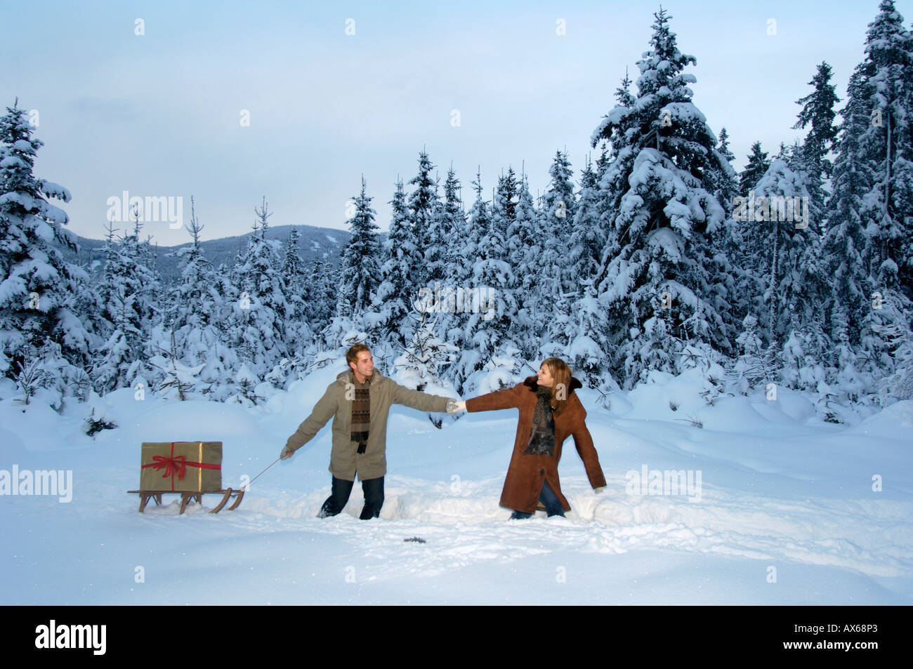 Coppia giovane che porta regali di Natale sulla slitta nella neve Foto Stock