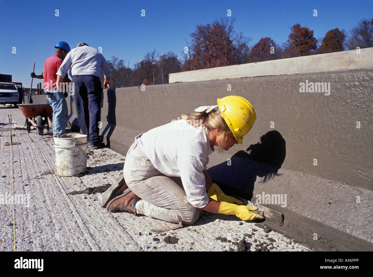 Costruzione femmina lavoratore la levigatura calcestruzzo bagnato su nuovo Interstate Highway barriera mentre i lavoratori di sesso maschile esaminare barriera Foto Stock