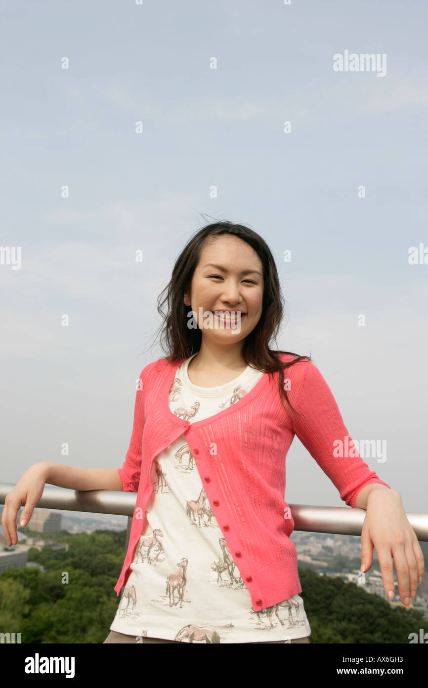 Una giovane donna di cuore sorride alla telecamera come essa si erge contro la ringhiera Foto Stock