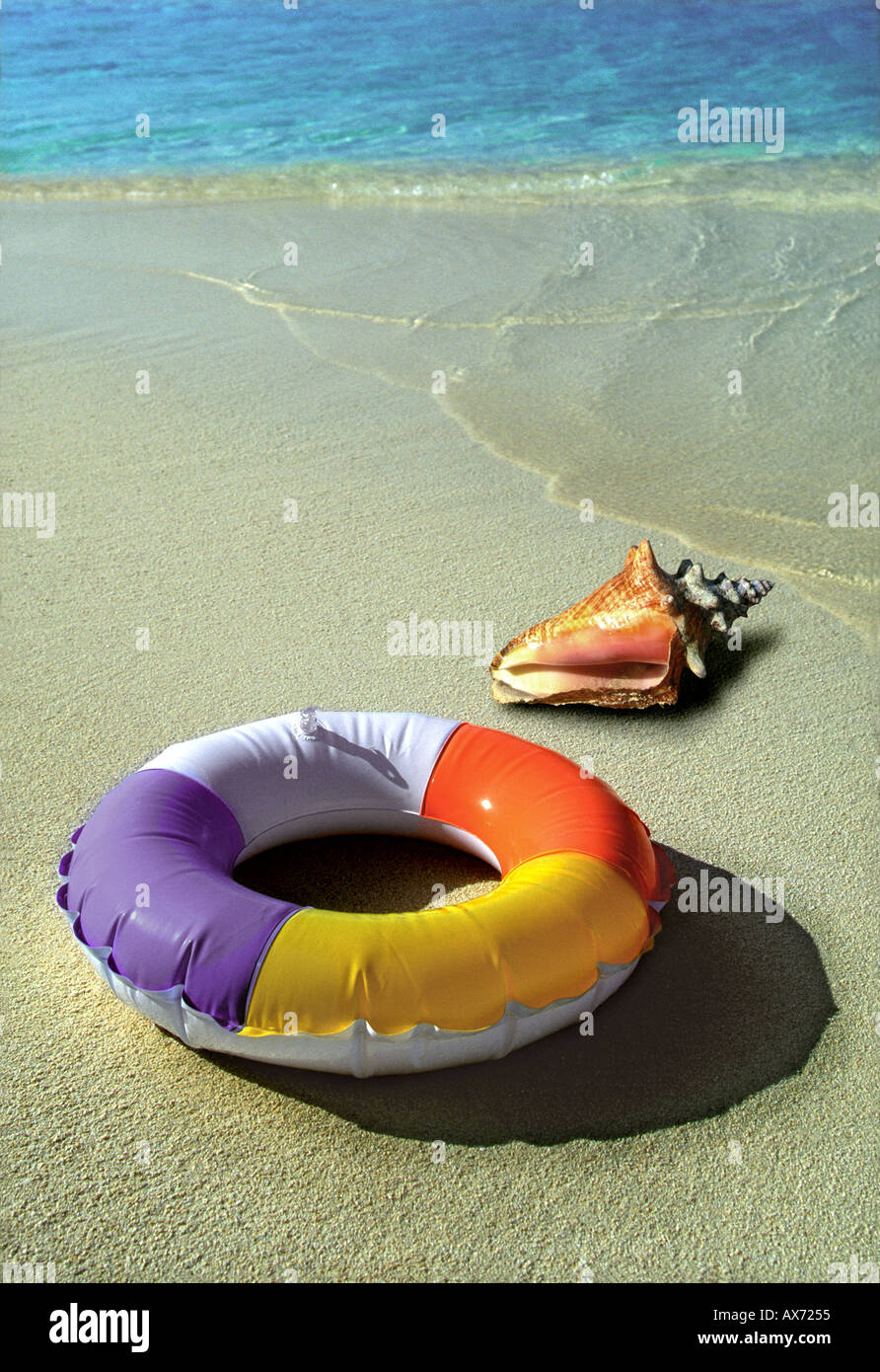 Piscina gonfiabile anello e conchiglia di mare sulla spiaggia di sabbia con mare blu sullo sfondo Foto Stock