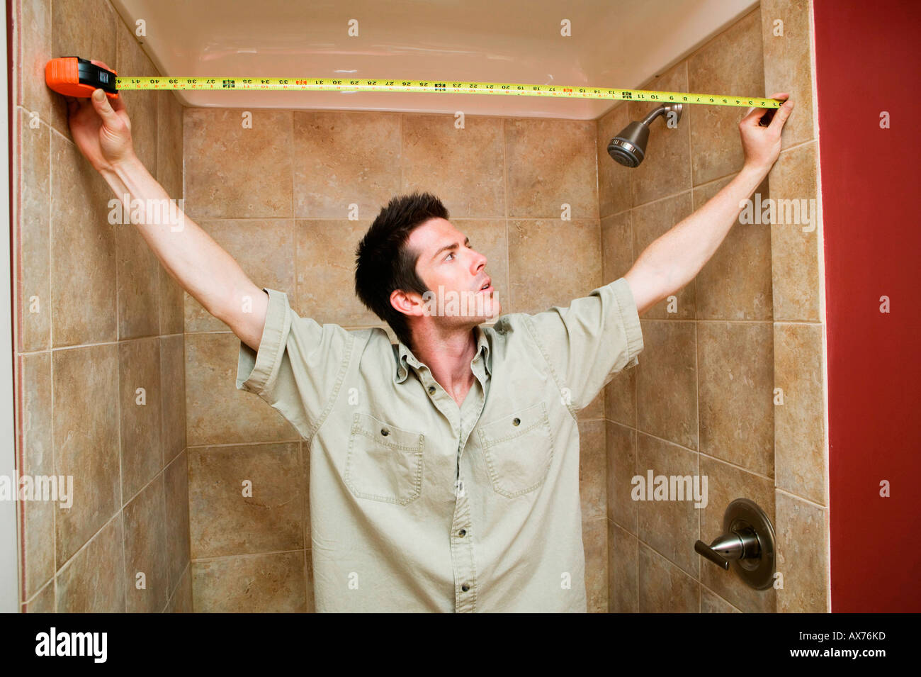 Giovane uomo a misurare la larghezza del bagno con un nastro di misurazione Foto Stock