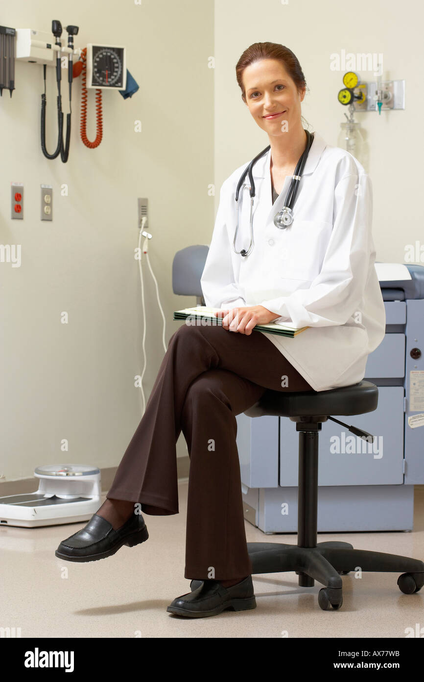 Medico donna seduta su uno sgabello e sorridente Foto Stock