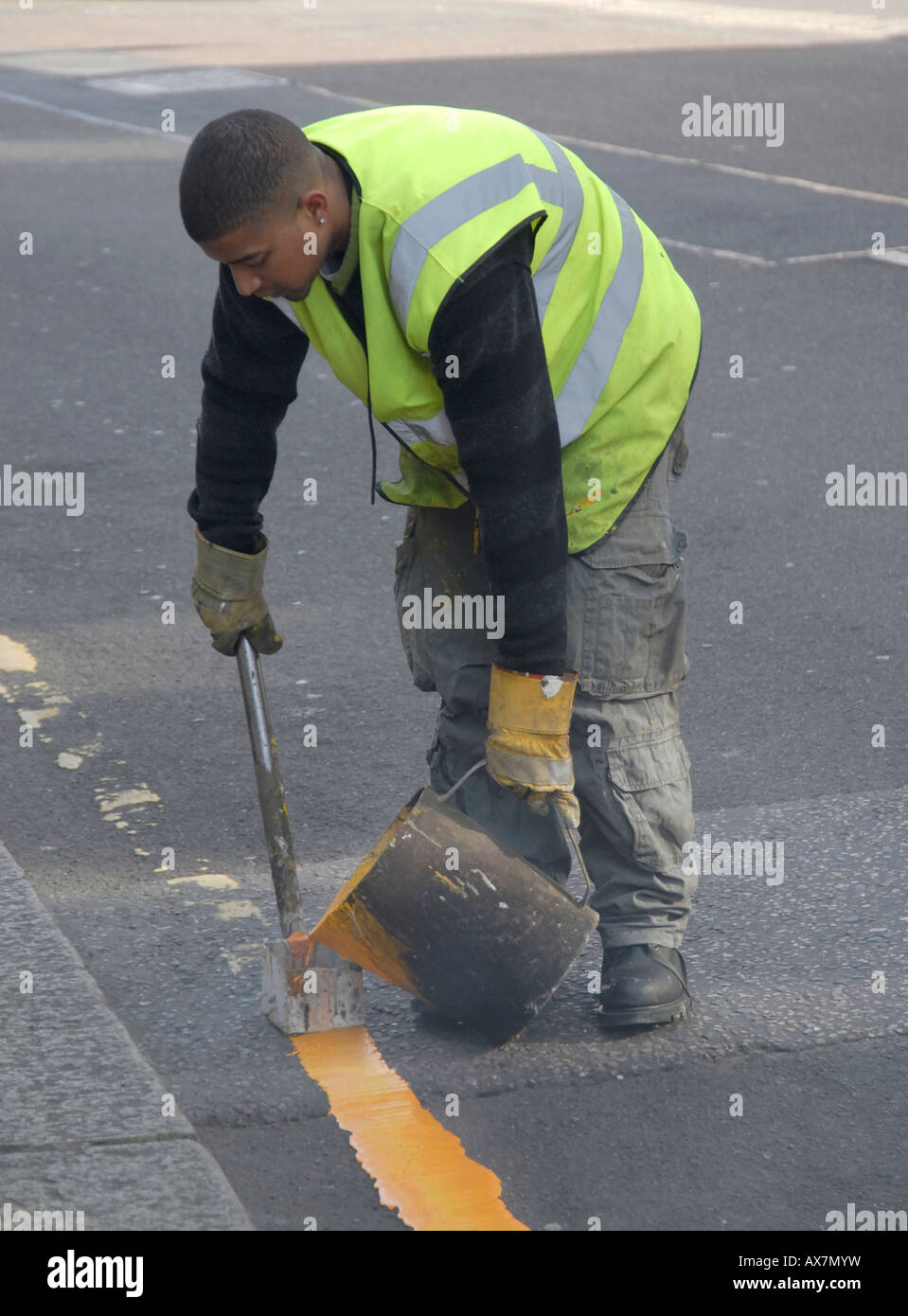 Giovane pittura a mano singola linea gialla sulla strada con bollitore di acqua calda di vernice e utensile di marcatura, Cheam, a sud di Londra - Inghilterra Foto Stock