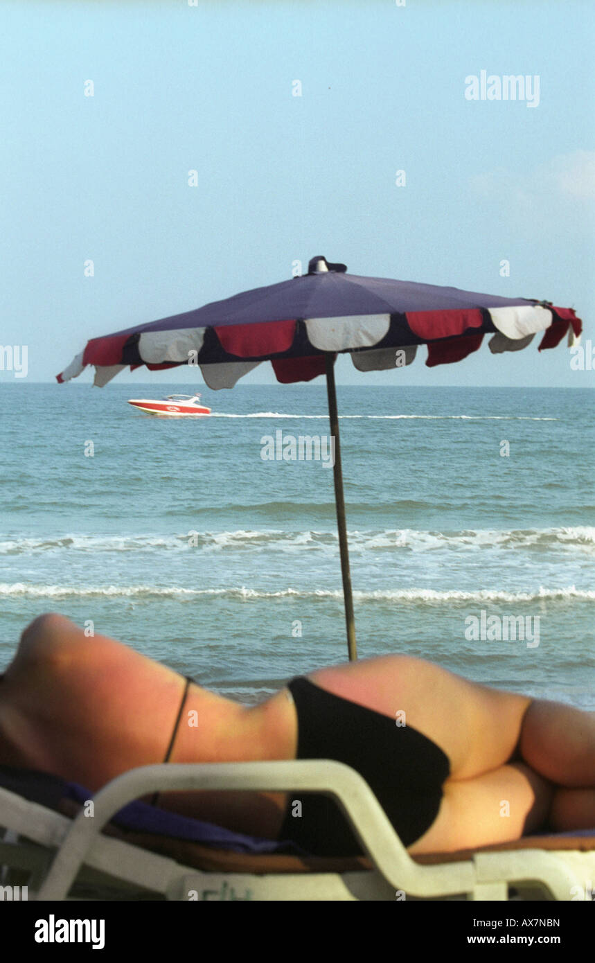 Una donna sdraiata su una sdraio sulla Chaweng Noi Beach, Koh Samui. Di fronte al mare con barca veloce racing in passato la distanza Foto Stock