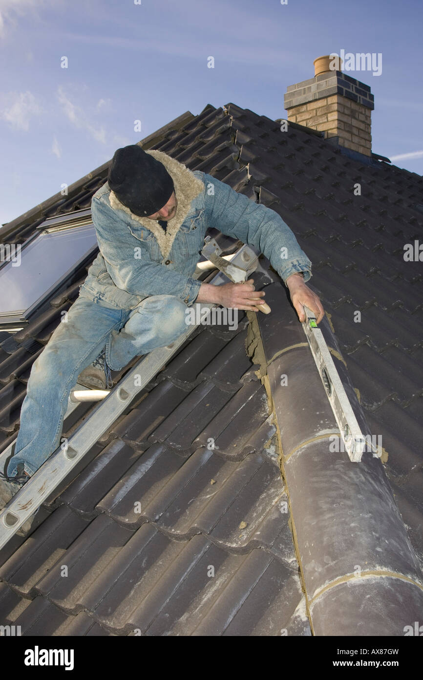 Builder con livello di spirito colmo di montaggio tegole di un tetto di una casa nuova Foto Stock
