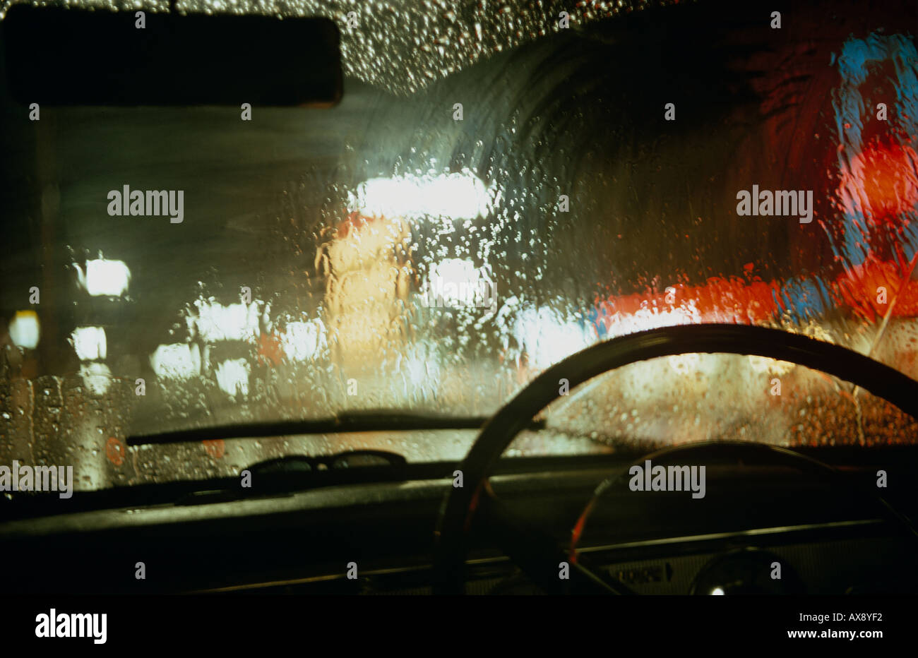 Forte pioggia sul parabrezza della vettura parcheggiata durante la notte con le luci urbane al di là. Inghilterra, Regno Unito. Foto Stock
