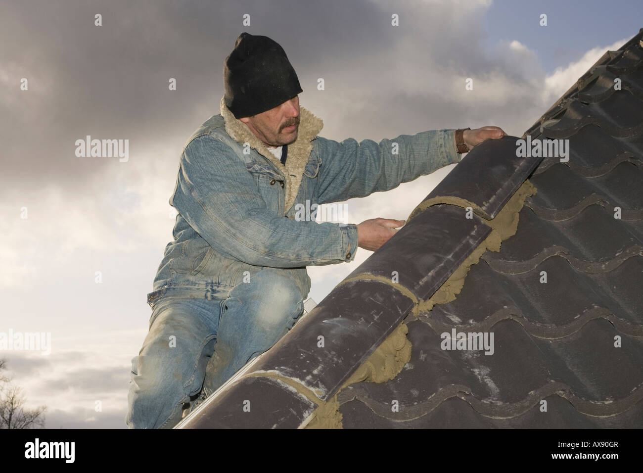 Un costruttore di montaggio tegole di colmo di un tetto di una casa nuova Foto Stock