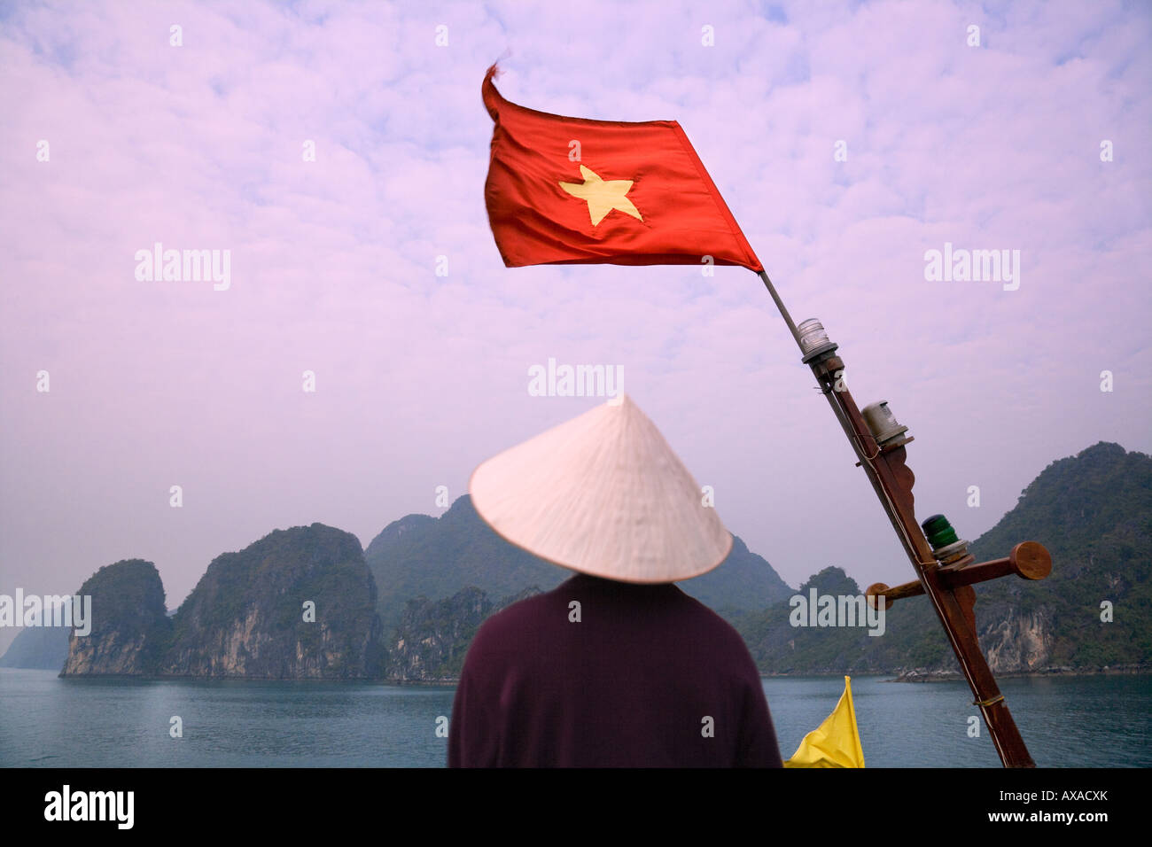 Ragazza con cappello conico su una barca di posta indesiderata con bandiera nazionale e del carso isole nella baia di Halong Vietnam Foto Stock