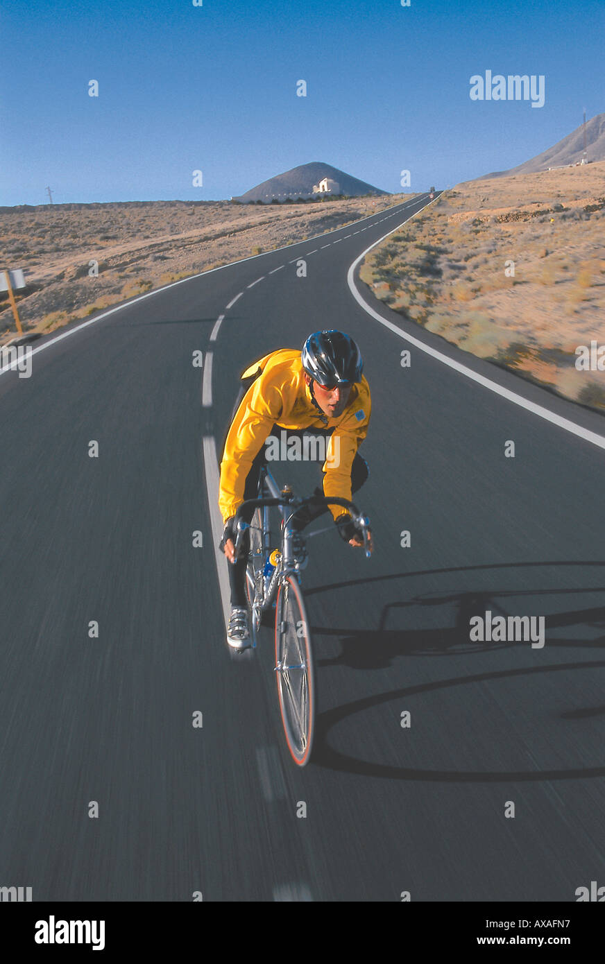 Un uomo su una bici da corsa a cavallo, lungo una strada di campagna, Fuerteventura, Isole Canarie, Spagna Foto Stock