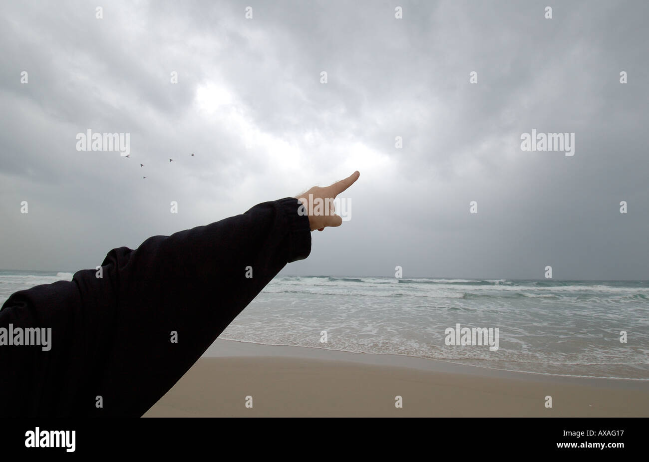 La mano di una persona che indica un cielo tempestoso e coperto sopra la spiaggia del Mar Mediterraneo. Israele Foto Stock