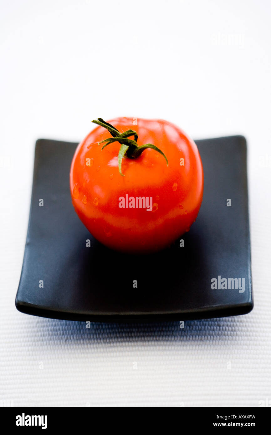 Uno rosso pomodoro su un quadrato nero piastra orientali Foto Stock