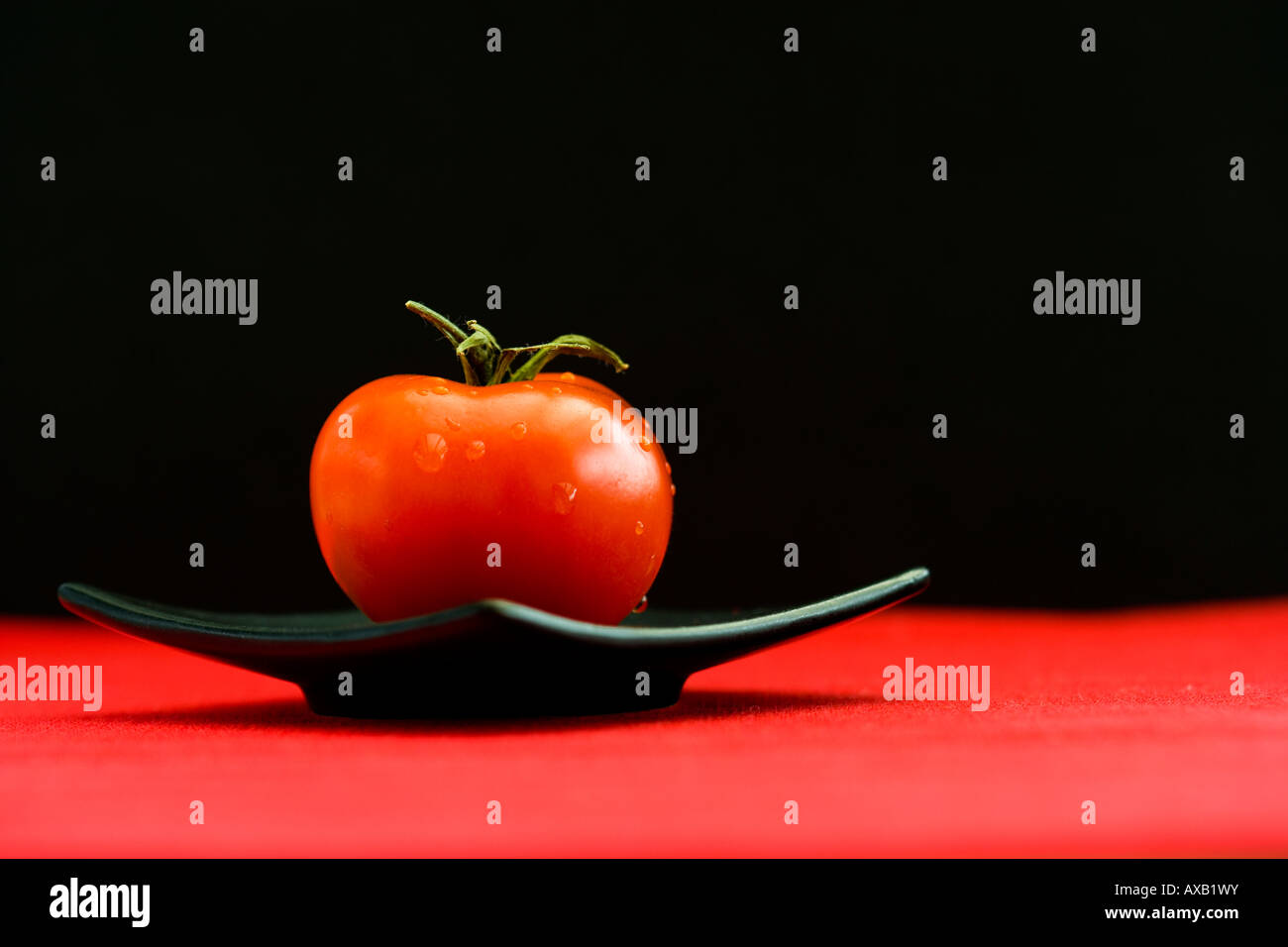 Uno rosso pomodoro su un quadrato nero piastra orientali Foto Stock