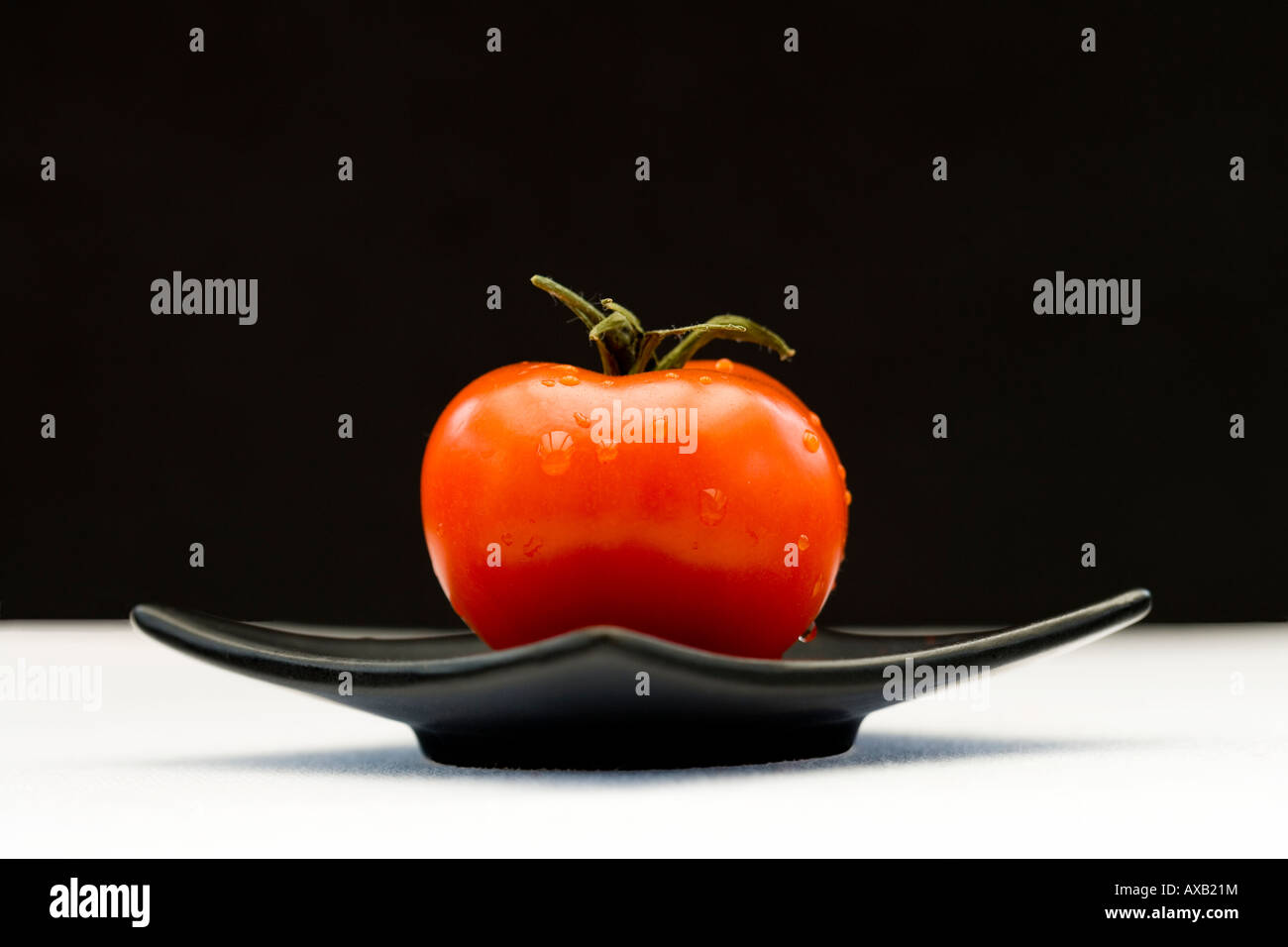 Uno rosso pomodoro su un quadrato nero piastra orientali Foto Stock