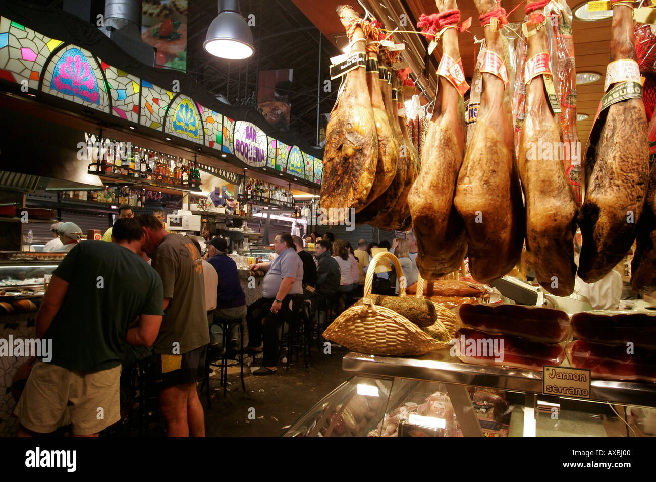 Barcelona Ramblas market hall la carne Boqeria stallo con prosciutto spagnolo Jammon prosciutto Serrano è appeso su garretti bodega persone Foto Stock