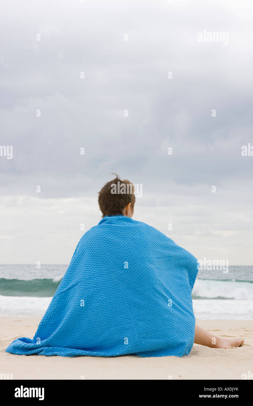 Donna con coperta blu seduto su una spiaggia Foto Stock