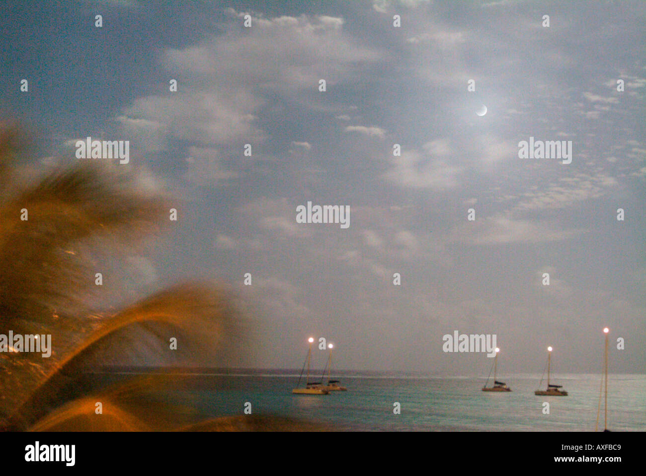 Chiaro di luna su una spiaggia caraibica come visto da un hotel balcone. Barche a vela con la loro testa del montante di luce può essere visto Foto Stock