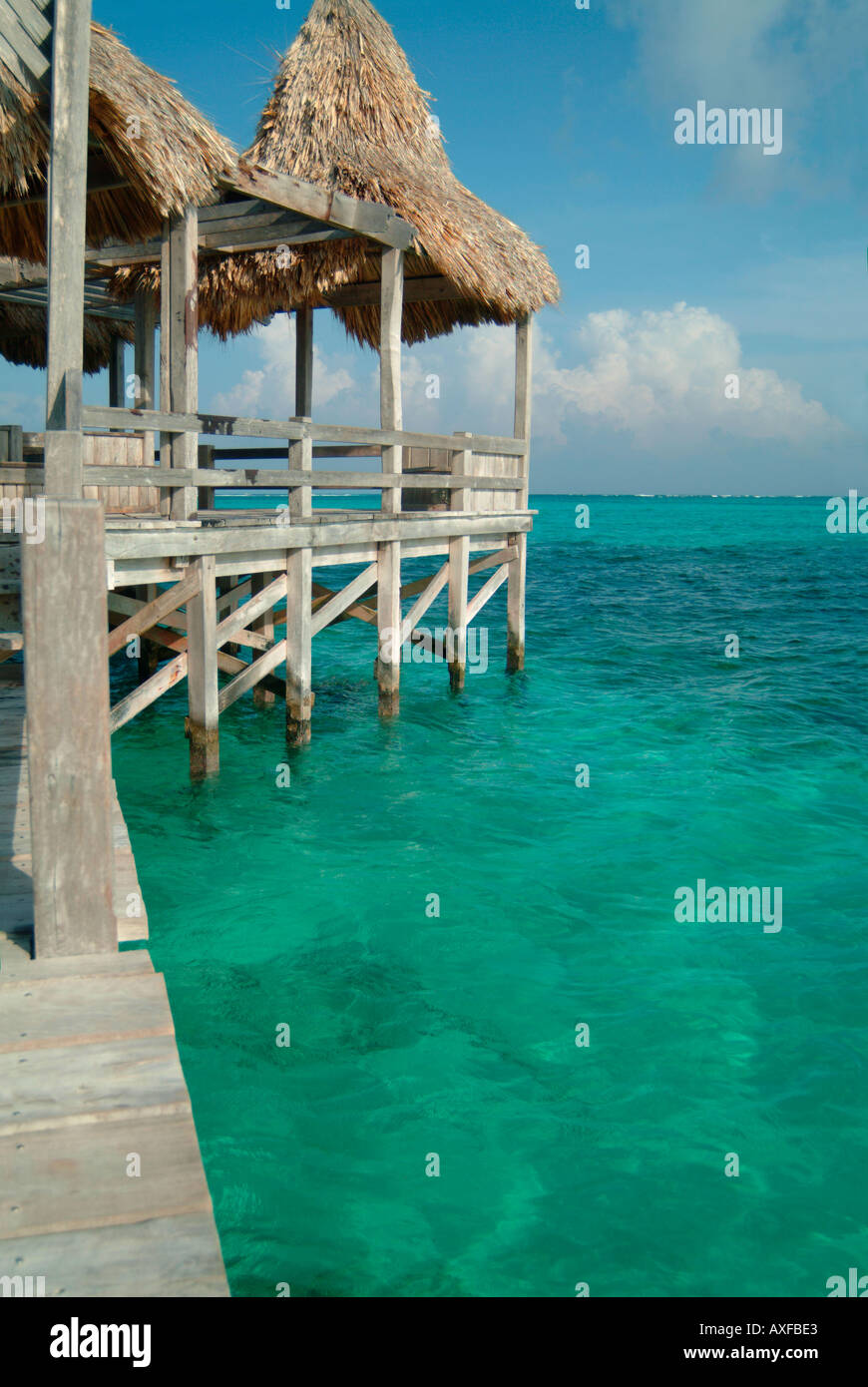 Un lungo molo in legno sporge nel Mar dei Caraibi da una spiaggia tropicale con tetti di paglia Foto Stock