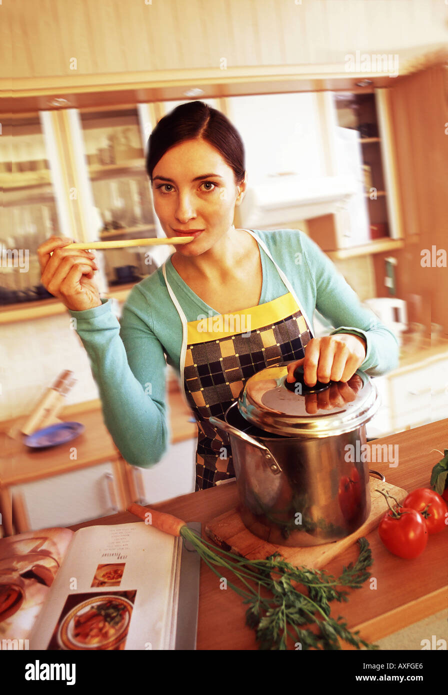 In ambienti interni cucina piana donna giovane ragazza 20 25 brunette grembiule stand tenere il cucchiaio di legno provate a mangiare fare cuocere soupe coperchio pentola salute foo Foto Stock