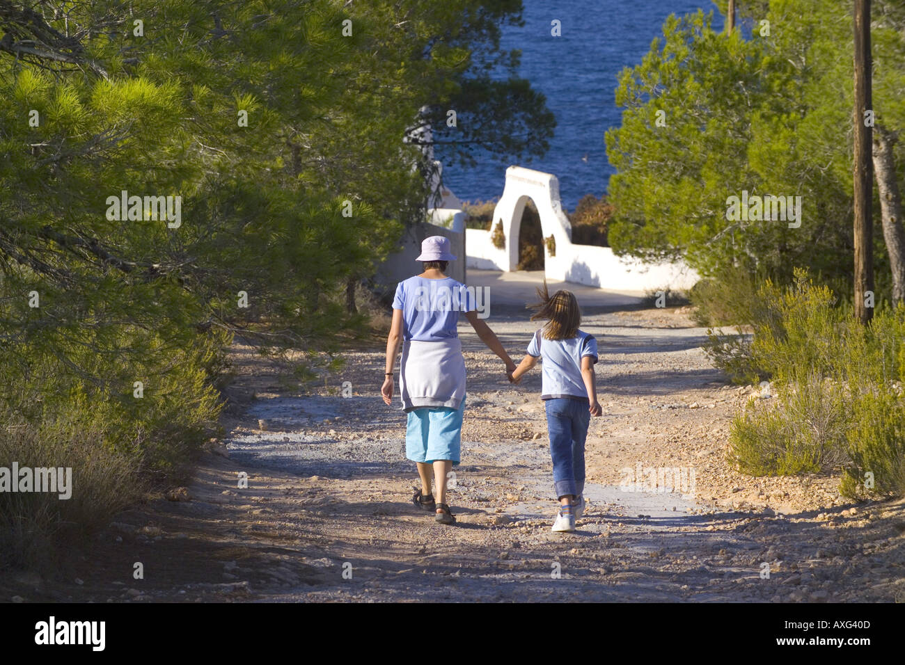 Spagna Ibiza madre e figlia a piedi lungo una pista polverosa verso il bianco edificio HACIENDA tenendo le mani Foto Stock