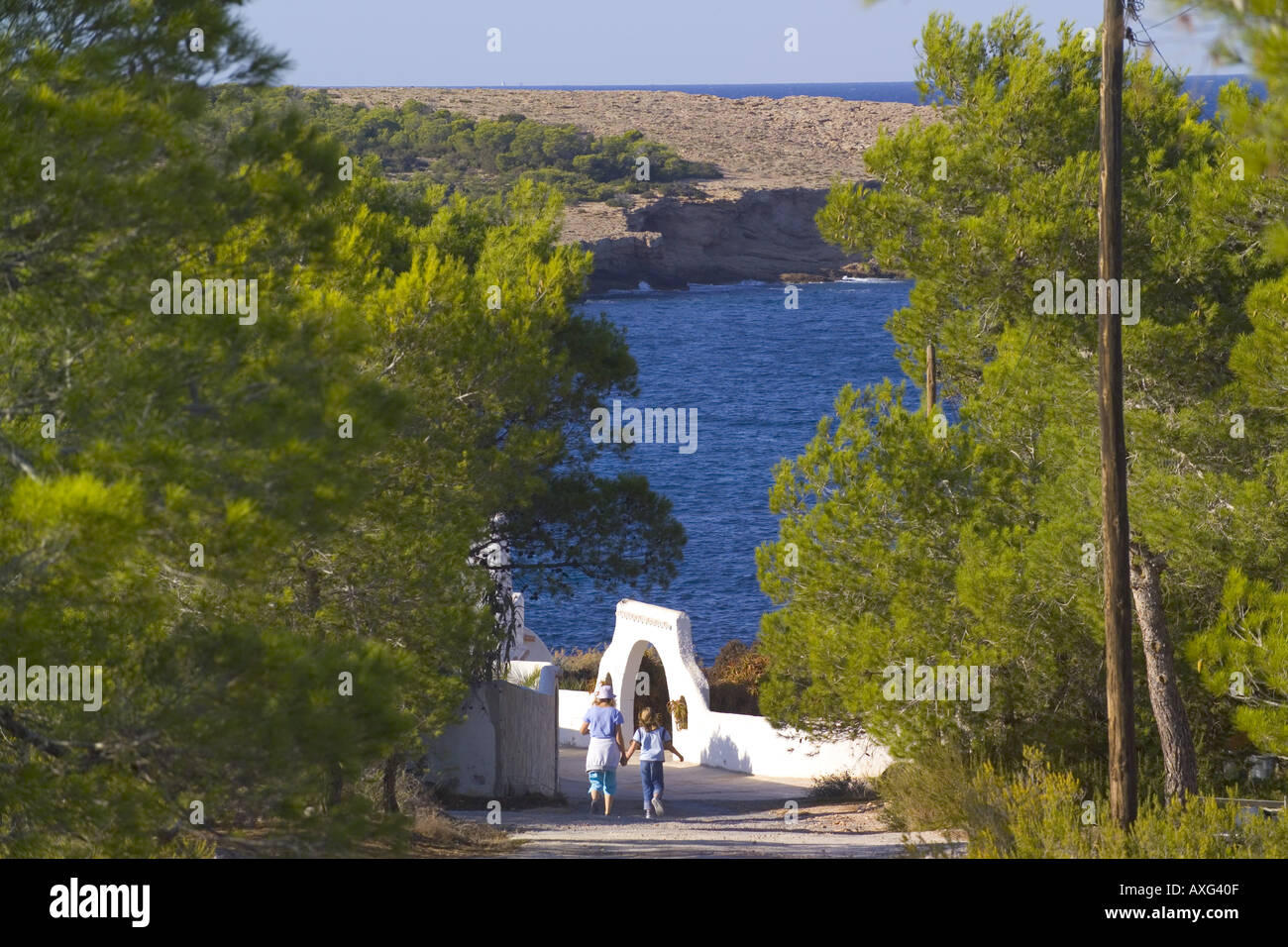 Spagna Ibiza madre e figlia a piedi lungo una pista polverosa verso il bianco edificio HACIENDA tenendo le mani Foto Stock