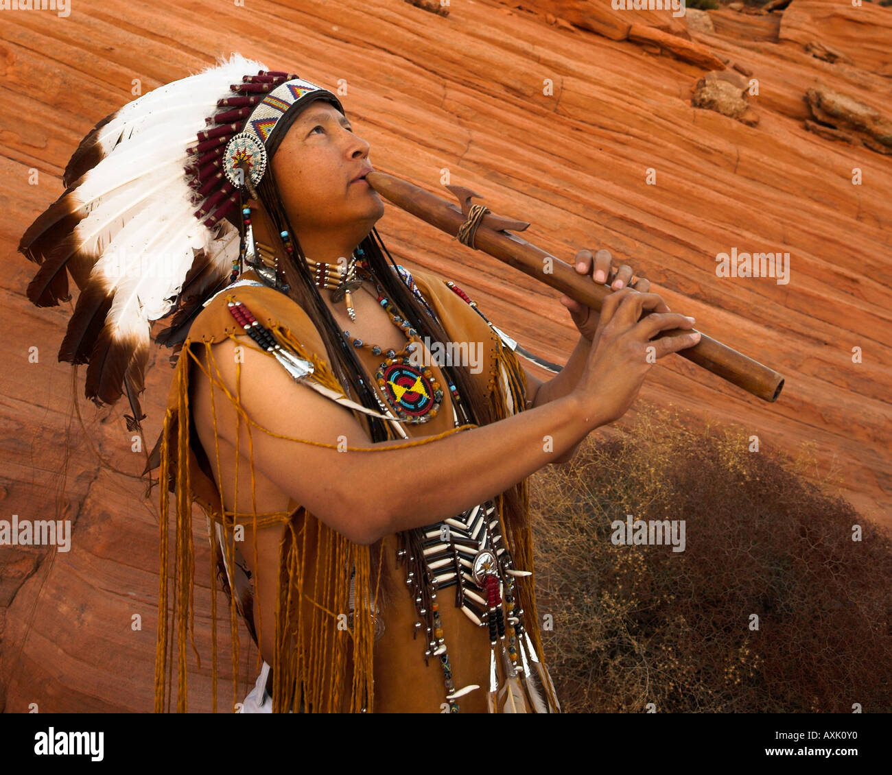 Native American Indian uomo persona con abito culturale uniforme di piume di acconciatura di suonare uno strumento musicale fischio avvisatore acustico Foto Stock