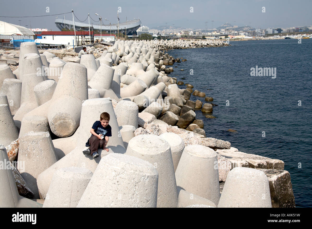 Giovane ragazzo in arrampicata sulla parete del mare difese da Mikrolimano con pace e amicizia al di là dello stadio nel porto del Pireo o Pireo ad Atene Gree Foto Stock