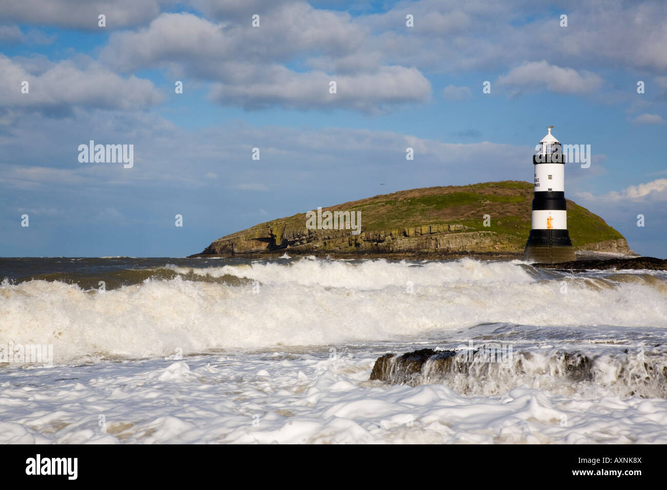 Mare mosso in tempo ventoso con Penmon faro (Trwyn Du) e onde in primo piano sulla costa rocciosa con Puffin Island. Punto Penmon Anglesey Wales UK Foto Stock