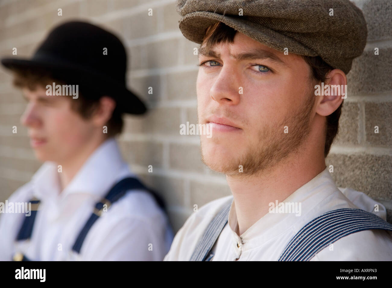 Gli uomini in vecchio stile abbigliamento in piedi contro un muro di mattoni Foto Stock