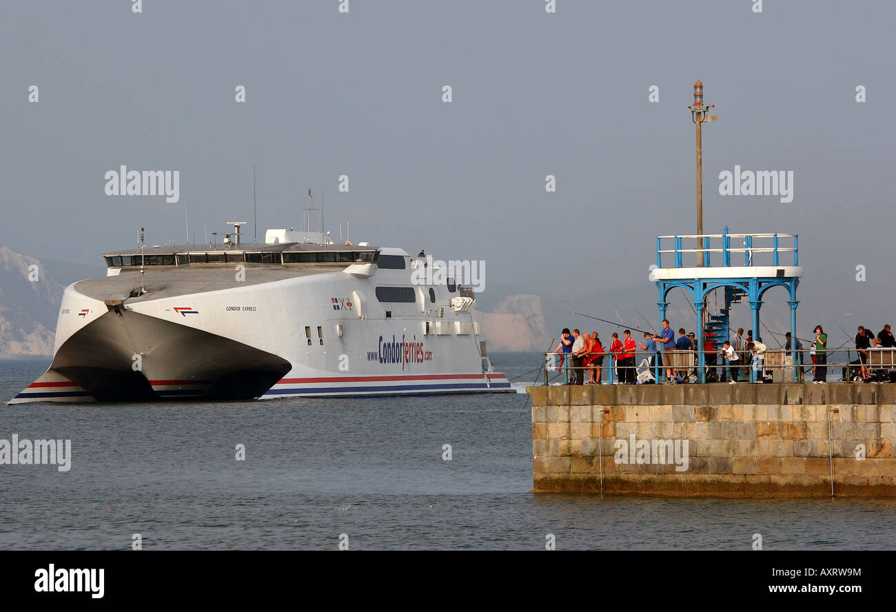 Condor Express traghetto dalle Isole del Canale entra nel porto di Weymouth guardato da pescatori pesca dal molo di pietra Foto Stock