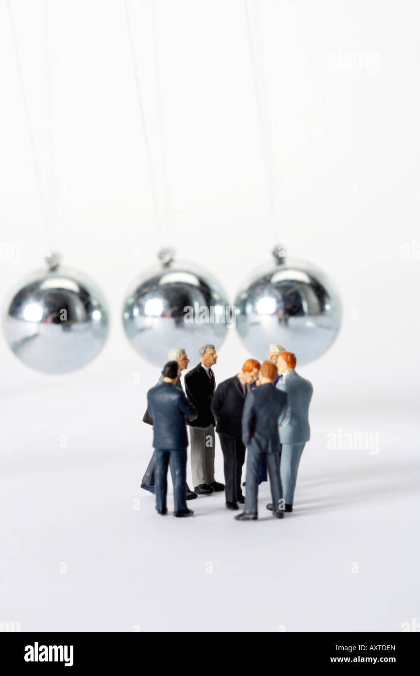 Gruppo di uomini di affari di statuette in piedi in cerchio, di Newton culla in background Foto Stock