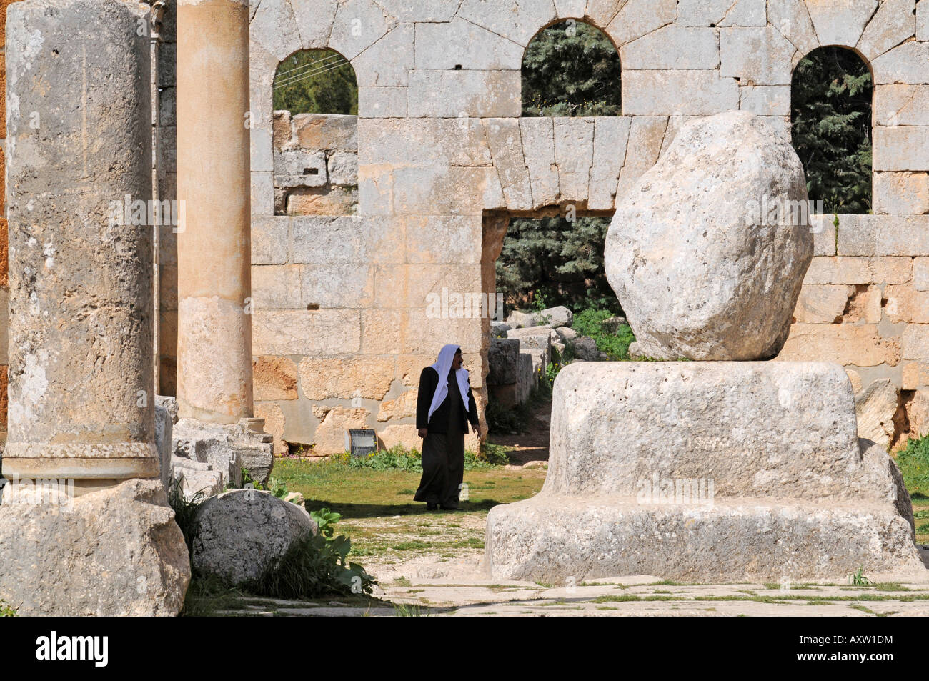 Un uomo arabo a piedi vicino al pilastro originale utilizzato da St Simeon Stylite a predicare in St Simeon basilica, Siria. Foto Stock