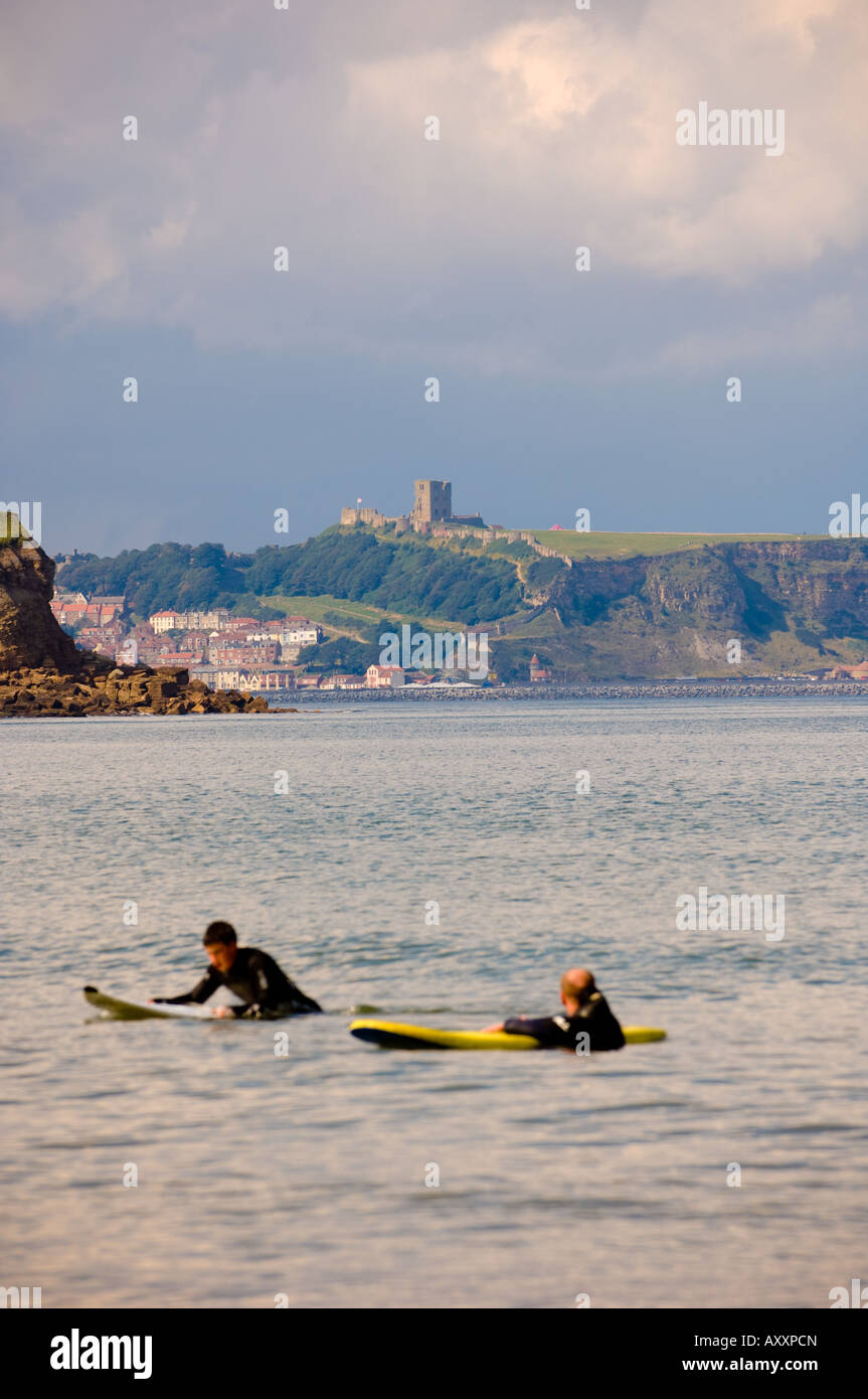 2 surfisti maschi sono parzialmente sommersi nel mare a Cayton Bay North Yorkshire UK con Scarborough sullo sfondo Foto Stock