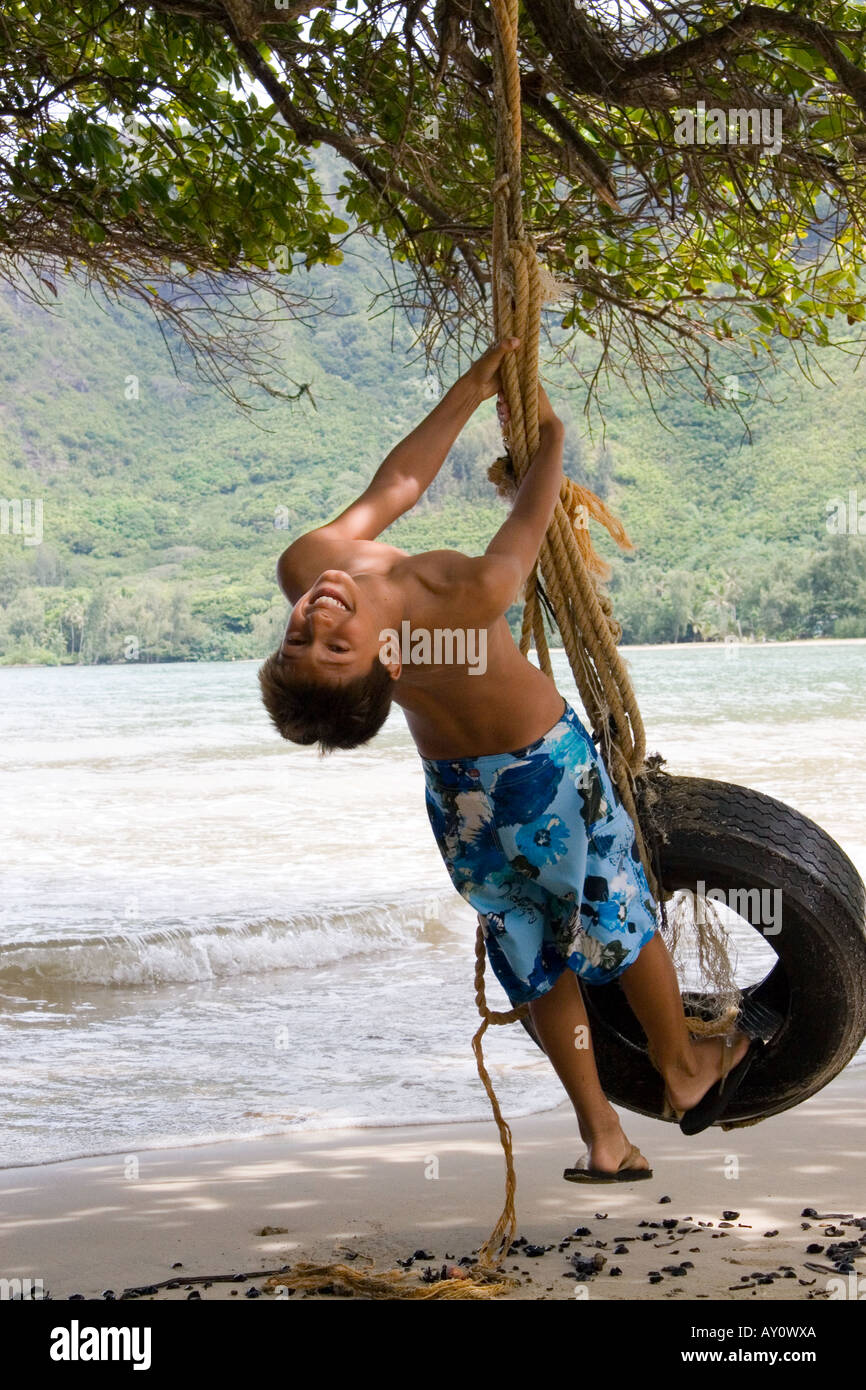 Ragazzo basculante in un pneumatico (pneumatico) swing sulla spiaggia in Oahu, Hawaii Foto Stock