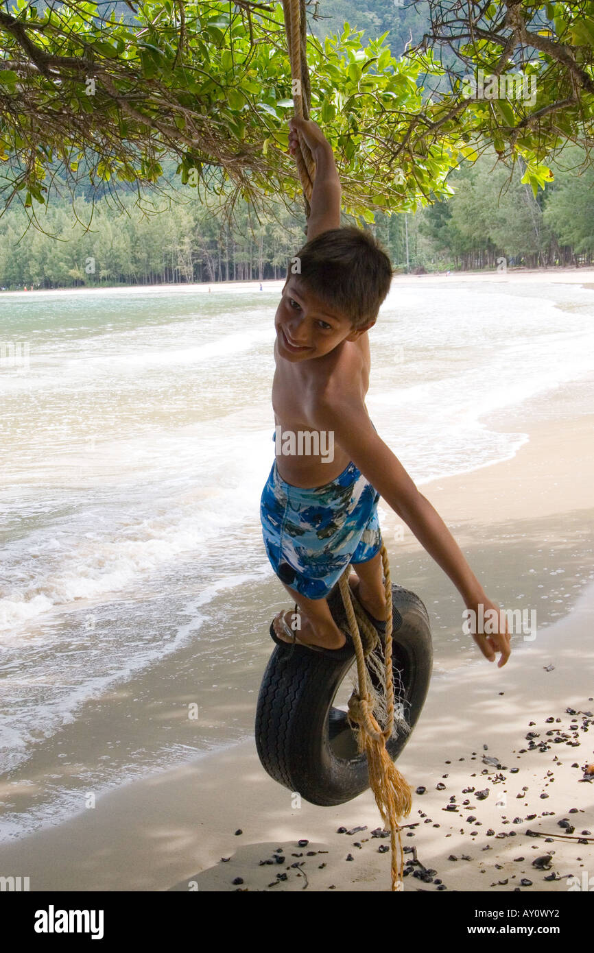Ragazzo basculante in un pneumatico (pneumatico) swing sulla spiaggia in Oahu, Hawaii Foto Stock