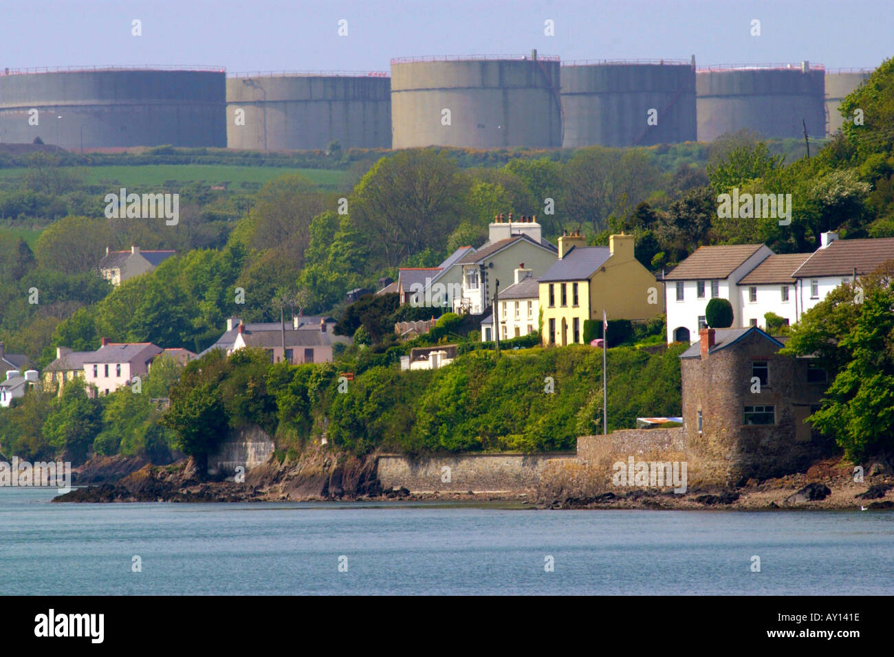 Villaggio di Llanstadwell dominato da grandi serbatoi di stoccaggio di una raffineria di petrolio Pembrokeshire Wales UK Foto Stock