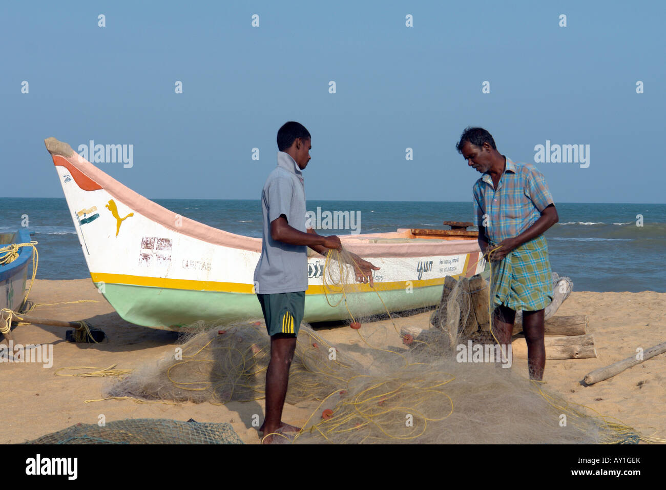 Due pescatori indiani di controllare le loro reti con tradizionale barca da pesca sulla spiaggia di mamallapuram Foto Stock