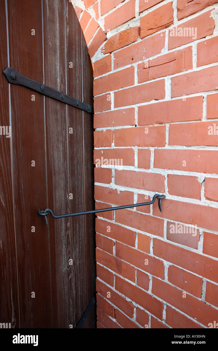 Il legno porta a porta con grande gancio in ferro tenendo lo sportello aperto. Rosso di parete di mattoni di ferro con occhiello in metallo Foto Stock