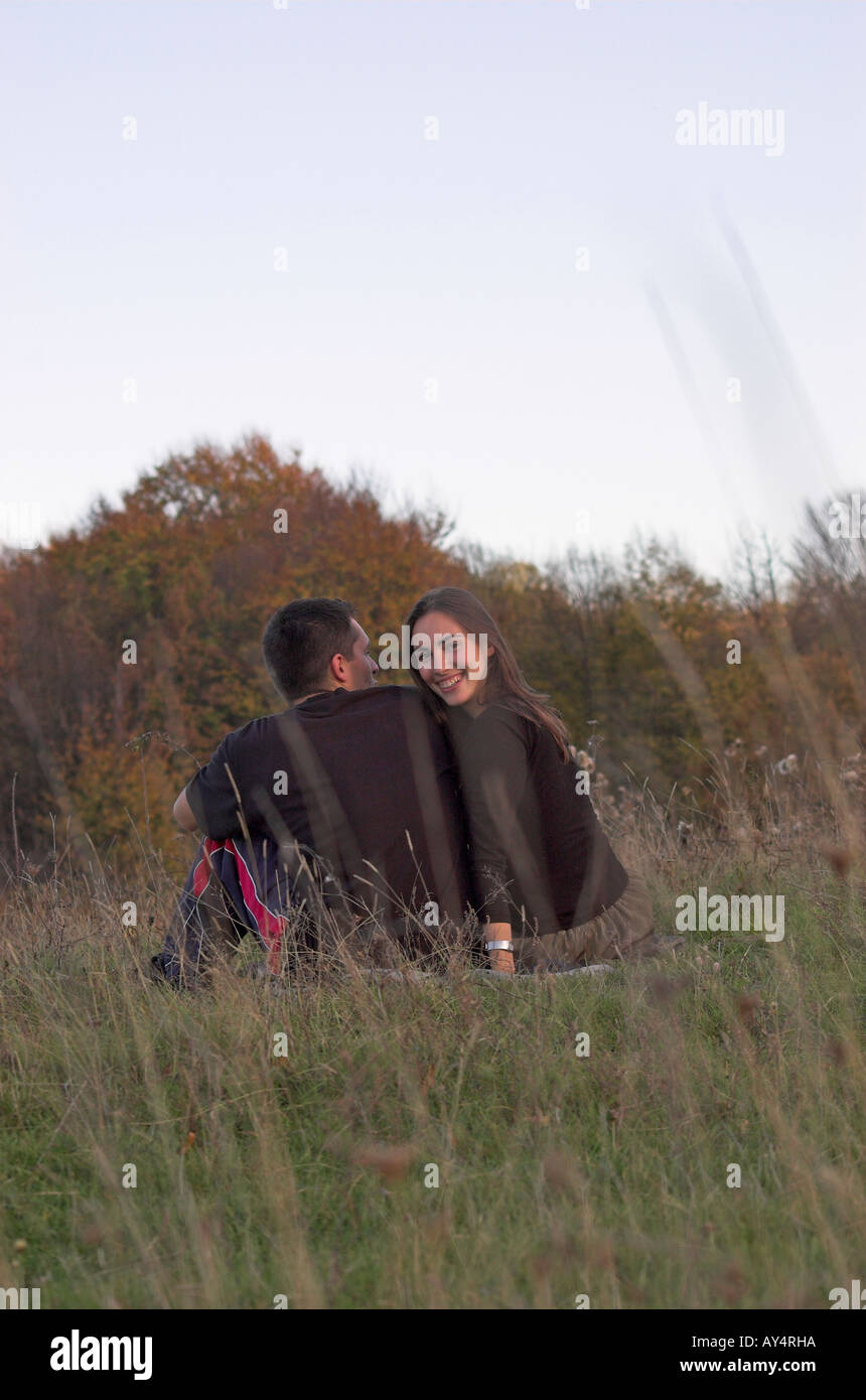 Coppia giovane seduto nel campo vista posteriore donna sorride guardando la fotocamera Foto Stock